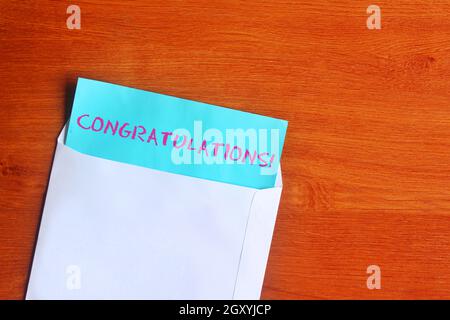 Top view image of blue paper with text CONGRATULATIONS! and white envelope on wooden background. Stock Photo