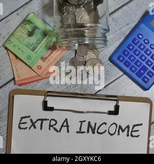 Top view of coins, banknotes, calculator and text EXTRA INCOME Stock Photo