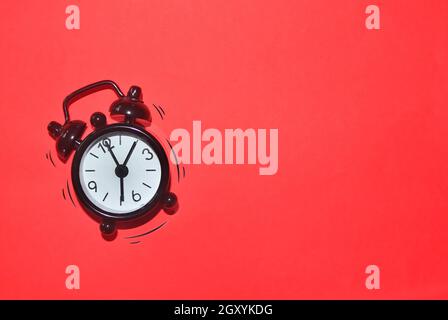 Black alarm clock on red background with loud and vibrating effect. Stock Photo