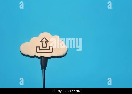 White cloud with upload icon connect to black cable on blue background. Copy space for text Stock Photo