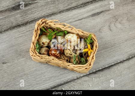 Table top view - square basket with quail eggs and some green leaves placed on gray wood desk. Stock Photo