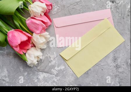 Tulips and envelopes on grunge grey background. Spring flowers blooming, fresh floral decoration for greeting, green freshness, romantic gift Stock Photo