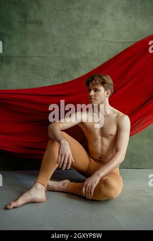 Male ballet dancer, dancing studio, grunge wall and red cloth on background. Performer with muscular body, grace and elegance of movements Stock Photo