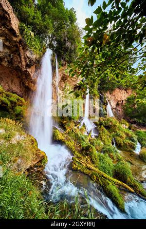 Vertical of large waterfalls over cliffs into lush green plants Stock Photo