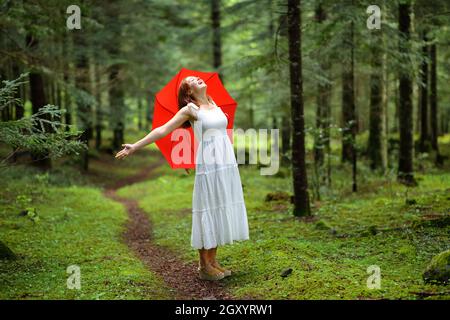 Excited woman with red umbrella celebrating vacation in a forest under ...