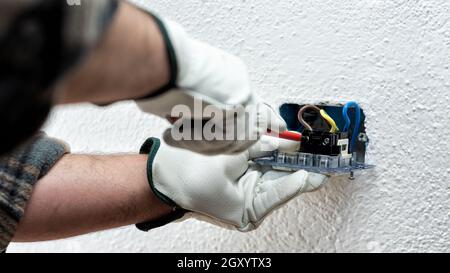 Electrician worker with screwdriver fixes electrical cables in the terminals of the socket of an electrical system. Working safely with protective glo Stock Photo
