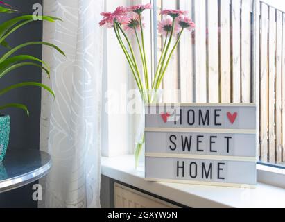Sign Home sweet home text on lightbox ,windowsill near window with pink flowers, decorative frame modern interior background, stylish house cozy corne Stock Photo