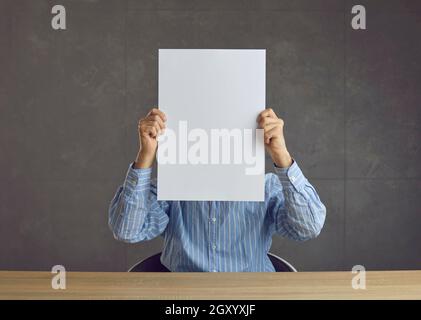Unknown man holds a white sheet of paper in front of his face with a blank space for text. Stock Photo