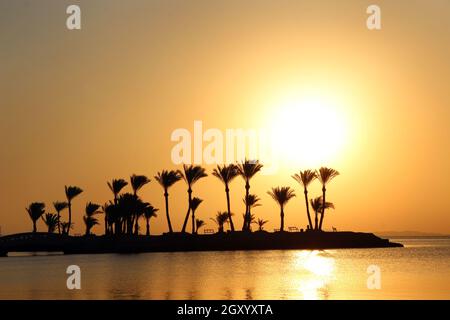 Beautiful place for privacy. Sunset over island in sea. Bright sun during dawn over the sea. Island with silhouettes of palm trees in ocean. Summer va Stock Photo