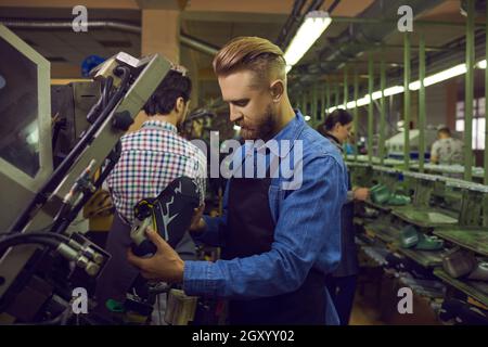 Male worker using industrial press while making new sneakers at footwear factory Stock Photo