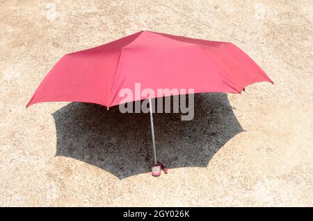UV umbrella in the summer sun. Red color beach umbrella blocking the sunlight. Shadow on the sandy floor. Sunbath tanning shade shadow background. Stock Photo