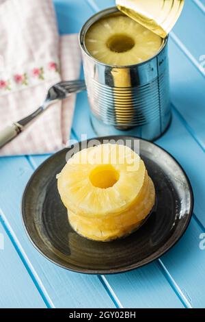Canned sliced pineapple fruit on plate on blue table. Stock Photo