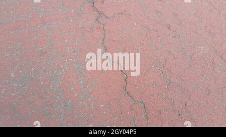 Red colored damaged road or paved pathway with crackes of different shpaes. Cracked texture with copy space for text and messages Stock Photo