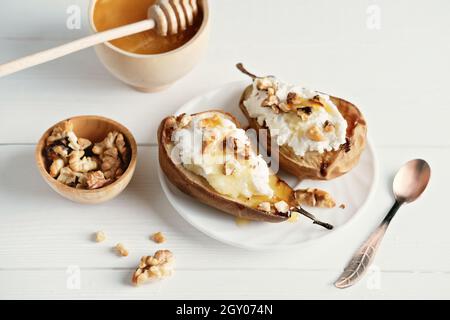 side view of halved baked pears with ricotta cheese and grilled walnuts. honey topping on dessert. light and tasty comforting fall food Stock Photo