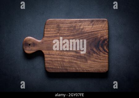 Black walnut handmade wooden chopping board. Handmade black walnut wooden cutting board on dark tone texture background. Stock Photo