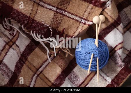 Blue ball of yarn with knitting needles on the background of a plaid in a cage. Stock Photo