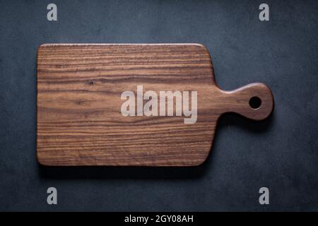 Black walnut handmade wooden chopping board. Handmade black walnut wooden cutting board on dark tone texture background. Stock Photo
