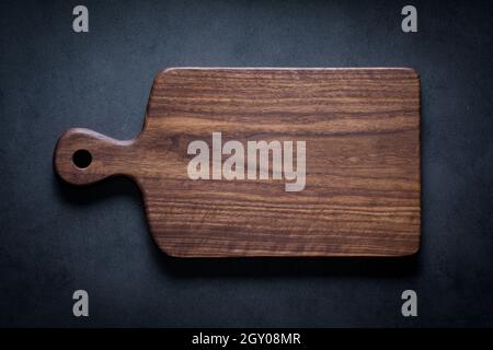 Black walnut handmade wooden chopping board. Handmade black walnut wooden cutting board on dark tone texture background. Stock Photo