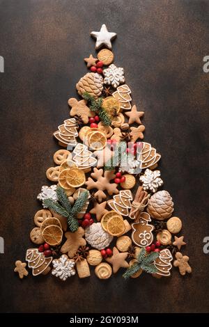 Creative sweet Christmas tree of glazed cookies, cinnamon, anise stars, berries, orange chips, on dark brown background. New Year greeting card. Top v Stock Photo