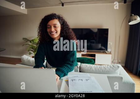 Adult mixed race female smiling while working on laptop sitting at kitchen counter top Stock Photo
