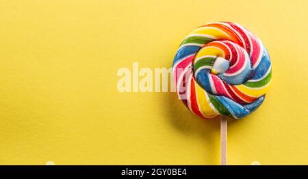 Sweet round lollipop with rainbow colour on the wooden stick with yellow background. Stock Photo