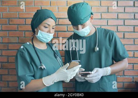 Two Doctor in green surgical gown hand working with smart phone. Medical technology network team meeting concept. Stock Photo