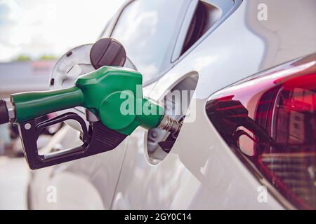 Green Handle pumping gasoline fuel nozzle to refuel. Vehicle fueling facility at petrol station. White car at gas station being filled with fuel. Tran Stock Photo