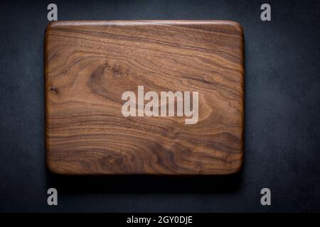 Black walnut handmade wooden chopping board. Handmade black walnut wooden cutting board on dark tone texture background. Stock Photo