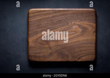 Black walnut handmade wooden chopping board. Handmade black walnut wooden cutting board on dark tone texture background. Stock Photo