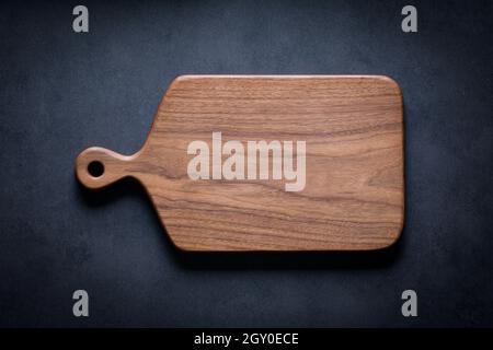 Black walnut handmade wooden chopping board. Handmade black walnut wooden cutting board on dark tone texture background. Stock Photo