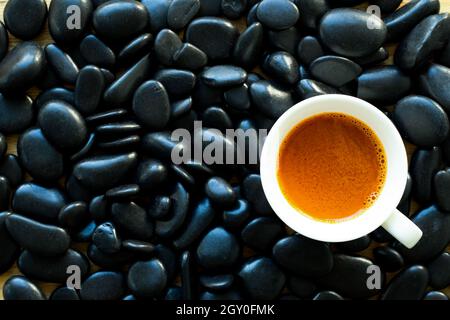 Top view of coffee cup on black stones. The coffee cup is white. Stones in the background are black and glossy. Stock Photo