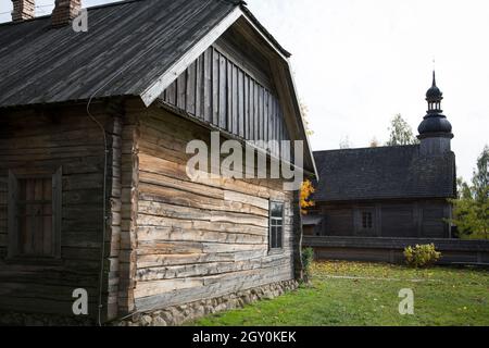 An old rustic wooden hut. In the background there is a rustic wooden church. Stock Photo