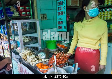 Female street vendor selling deep fried fish balls, skewered one day old chicks and other fast food. Baguio city, Philippines. Stock Photo