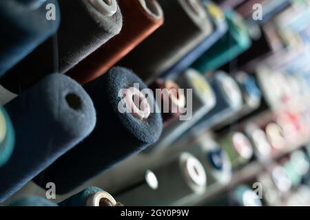 In a sewing workshop, many spools of thread of different colors hang on a metal wall. Tailoring concept. Stock Photo