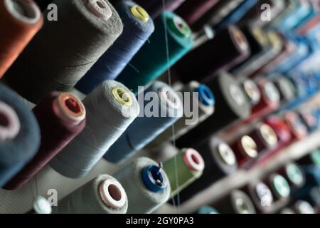 Sewing threads of different colors are installed on a metal wall and are in the sewing workshop. Manufacturing and material diversity concept. Stock Photo