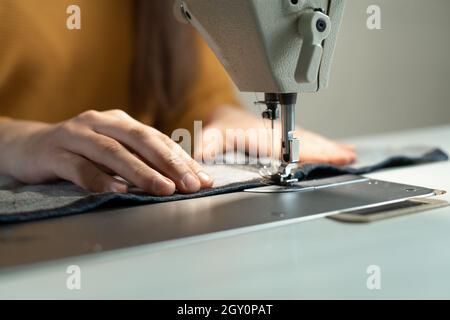 The girl's hands put the fabric under the needle in the sewing machine while making clothes. Sewing workshop work concept. Stock Photo