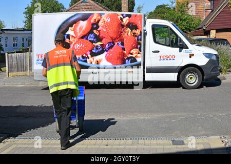 View of Tesco supermarket grocery driver high visibility staff uniform returns empty crates back to van from home delivery to online customer Essex UK Stock Photo