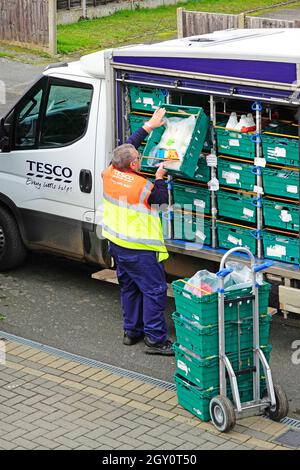 Tesco supermarket home delivery van open side of groceries in food crates & staff man driver unloading online grocery shopping onto trolley England UK Stock Photo