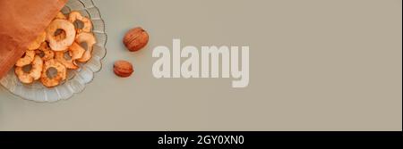Dried sliced apple chips in paper bag and walnuts - healthy snacks. Proper nutrition, healthy food concept. Top view. Extra wide banner. High quality Stock Photo
