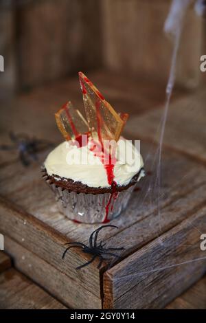 Halloween treat chocolate cupcake with white frosting impaled with glass shards that ooze red blood sauce Stock Photo