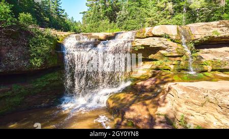 Close-up of large waterfall over cliffs with heavy moss on brown rocks Stock Photo