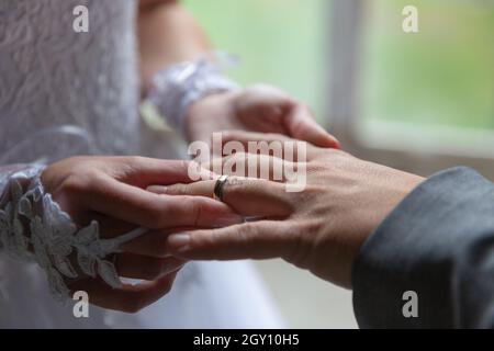 Bride putting the wedding ring on groom finger close up. Stock Photo