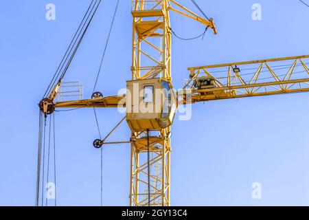 Yellow construction crane with cabin close-up against blue sky background. Concept of lifting of cargo, construction machinery and modern technology Stock Photo