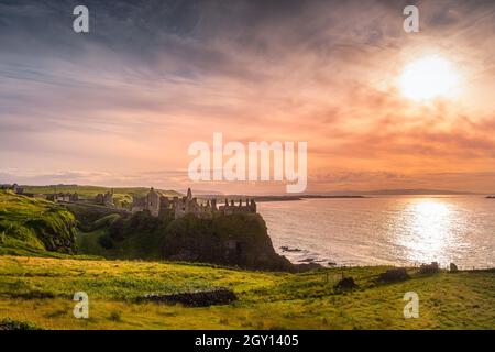 Dramatic sunset at medieval ruins Dunluce Castle perched on the cliff, Bushmills, Northern Ireland Filming location of popular TV show Game of Thrones Stock Photo