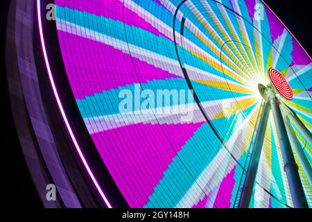 Ferris wheel fully lit up at night with pinks and blues and grays in a compass like design Stock Photo