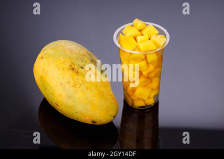 Ripe Mango cubes or cut piece arranged in a transparent glass with  mango placed beside on black color background. Stock Photo