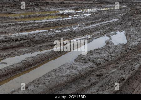 A broken rural country road after the rain. Puddles after rain on a dirt road. Clay, soil and puddles at cloudy day light after rain, autumn season. Stock Photo
