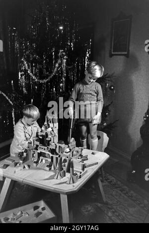 Zwei Jungen spielen am Weihnachtsabend mit den neuen Bauklötzen, Deutschland 1938. Two boys playing with the new set of toy blocks under the christmas tree, Germany 1930s Stock Photo