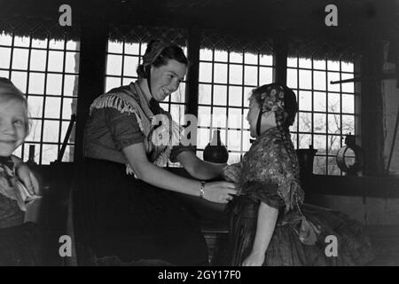 Eine Frau hilft einem kleinen Mädchen beim Anziehen der Tracht der Gegend um Ammerland bei Bad Zwischenahn im Oldenburger Land, Deutschland 1930er Jahre. A woman helping a little girl to wear traditional costume of Ammerland near Bad Zwischenahn at the Oldenburg area, Germany 1930s. Stock Photo