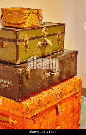 Stack of three antique trunks, red, black, and green, with a basket on top in yellowed lighting Stock Photo